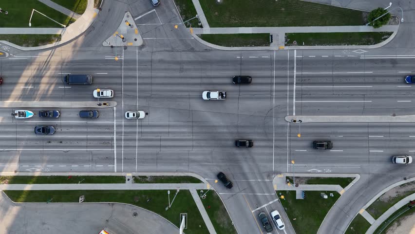 Drone aerial static view of a Winnipeg intersection, Manitoba, Canada. Cars travel through road lanes with traffic lights, sidewalks, grass areas, and surrounding buildings visible.