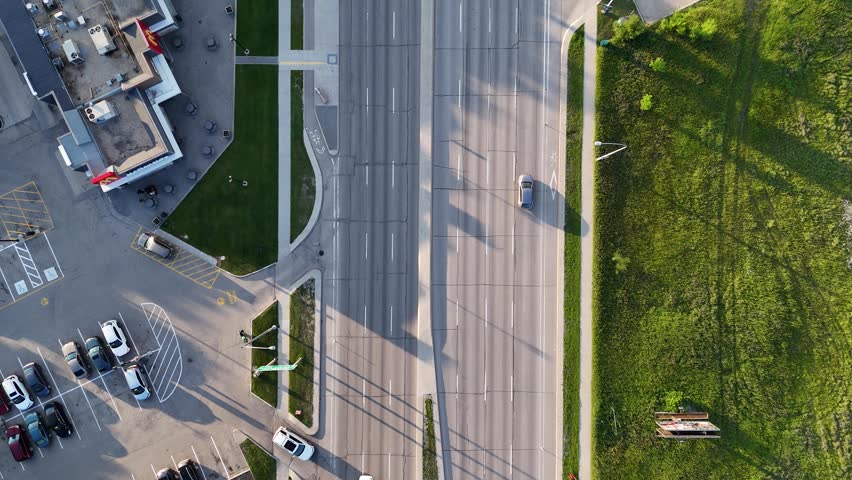 Drone aerial overhead view of Pembina Highway in Winnipeg, Manitoba, Canada. Camera moves forward above roadway showing cars, traffic lanes, sidewalks, grass areas, and buildings in summer.