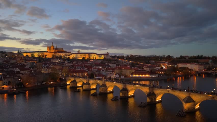 Aerial view of Prague Castle and Charles Bridge at dusk, illuminated by warm lights over the Vltava River in Prague, Prague, Czechia.