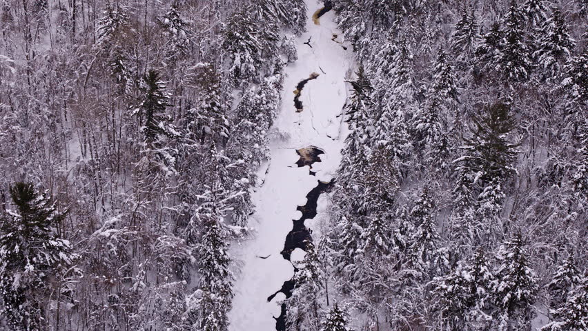 Aerial footage of a quiet winter river weaving through a frozen Northern Michigan forest.
