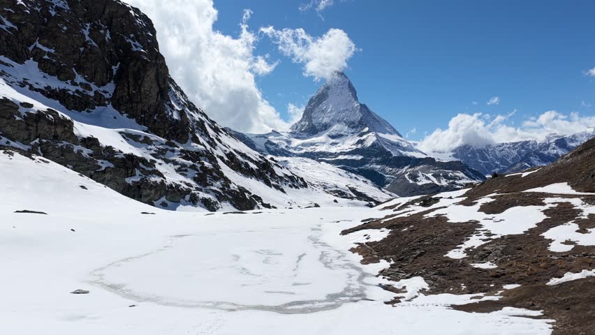 Aerial view of the iconic Matterhorn peak rising above snow-covered slopes and rocky terrain under a bright blue sky in Zermatt, Valais, Switzerland.