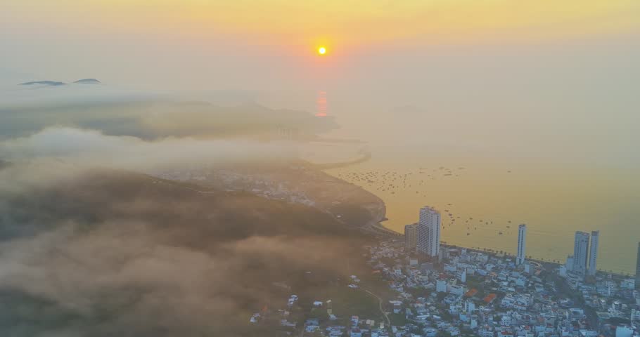 A breathtaking sunrise view over the mountains surrounding Nha Trang city, Vietnam. Where golden sunlight spreads across a sea of clouds. Rolling green hills emerge through drifting mist, while the distant city and coastline appear softly beneath the haze. The scene captures a magical blend of nature and urban landscape at dawn, creating a peaceful and dreamlike atmosphere.