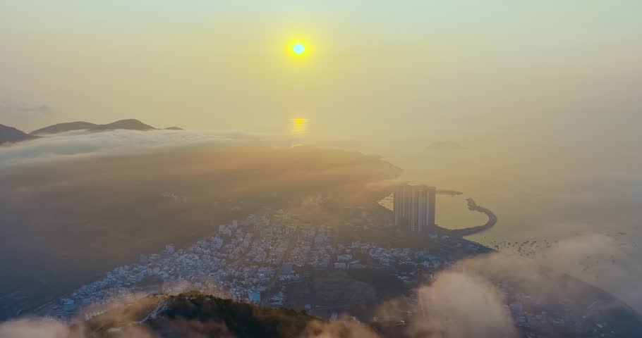 A breathtaking sunrise view over the mountains surrounding Nha Trang city, Vietnam. Where golden sunlight spreads across a sea of clouds. Rolling green hills emerge through drifting mist, while the distant city and coastline appear softly beneath the haze. The scene captures a magical blend of nature and urban landscape at dawn, creating a peaceful and dreamlike atmosphere.