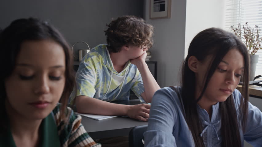 Caucasian teenage boy yawning and looking bored during school lesson while girls sitting in foreground. Perfect for educational marketing and student mental health campaigns