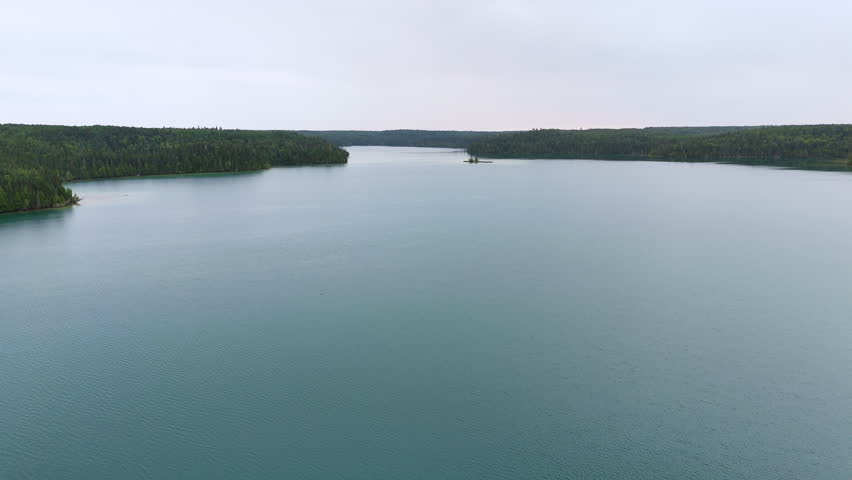 Aerial view of a calm turquoise lake in the northern Ontario wilderness, with pristine boreal forest stretching to the horizon over Big Skunk Lake.