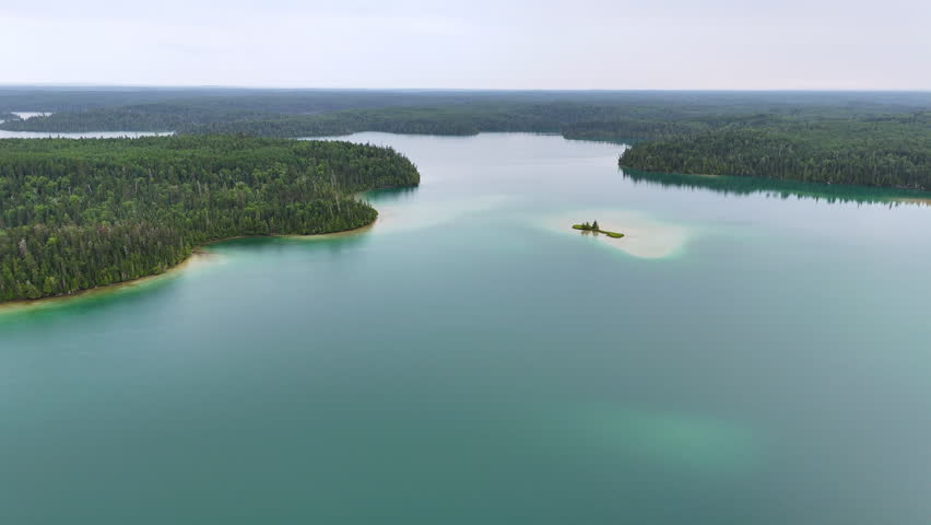 Aerial view of a picturesque sandy island surrounded by vibrant turquoise water on Big Skunk Lake in northern Ontario, with pristine boreal forest and the expansive lake in the background.