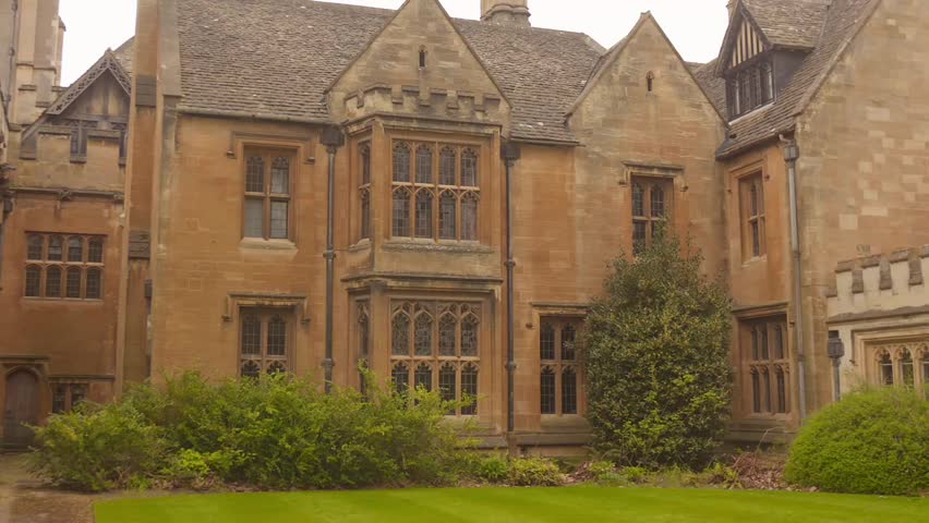Historic stone building with ornate windows and manicured lawn in college courtyard
