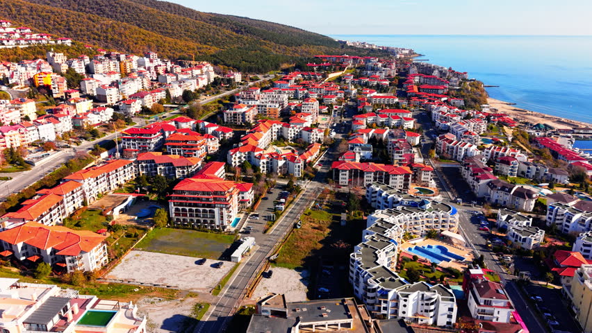 Elevated view of a seaside town along the mountains, Bulgaria. Red roofed buildings stretching toward a calm sea and beach.