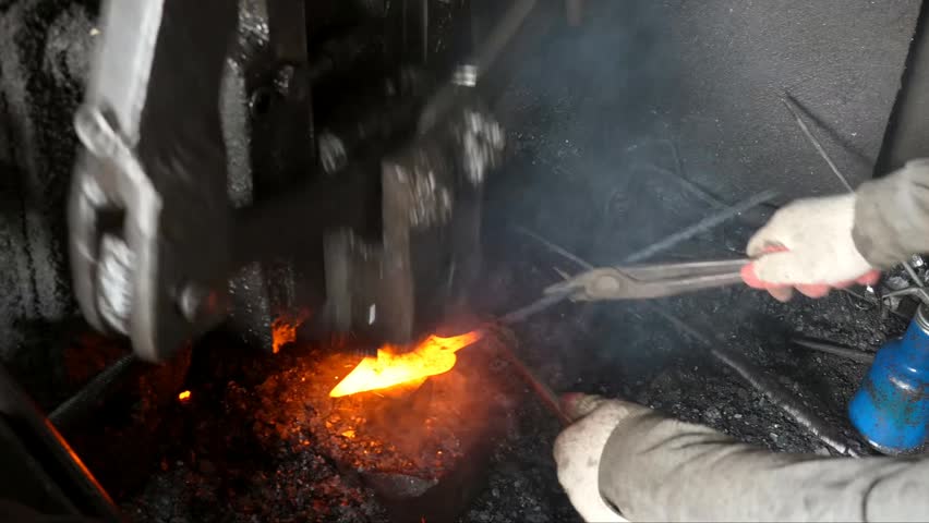 The blacksmith employs a powerful mechanical hammer to shape glowing metal on an anvil, followed by intense reheating within a coal fire furnace for further industrial forging operations.