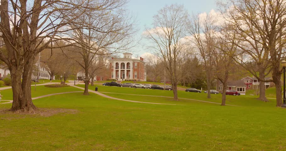 People walking on grassy park lawn with historic building and trees in springtime