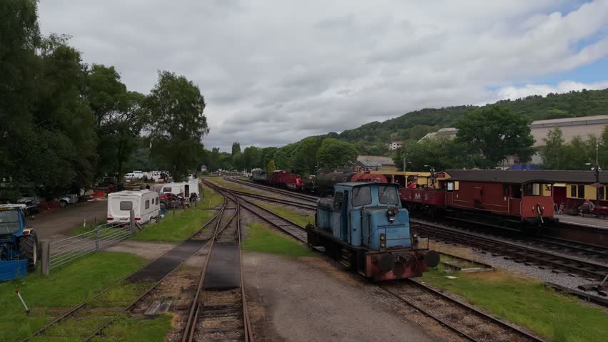 A train station with vintage carriages and festive market stalls, set amid trees and cloudy skies