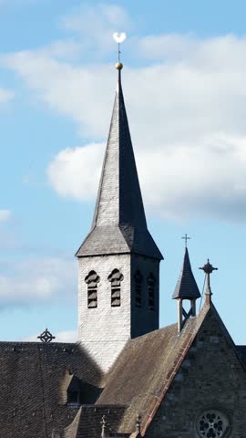 A vertical view of Altenberger Dom tall church spire under a blue sky with scattered white clouds
