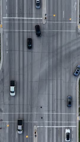 Vertical drone overhead view of a Winnipeg intersection, Manitoba, Canada. Drone slowly ascends above roadway showing cars, traffic lanes, sidewalks, grass areas, streetlights, and nearby buildings.
