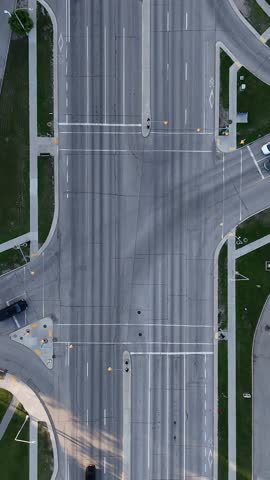 Vertical drone overhead close view of a Winnipeg intersection, Manitoba, Canada. Cars travel through road lanes with visible traffic lights, sidewalks, grass areas, and nearby buildings.
