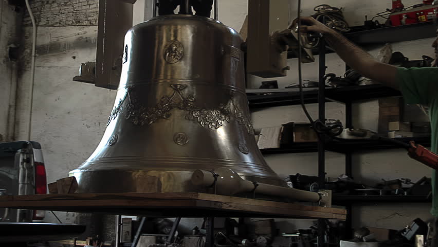 Worker Hand Moving Big Shiny Bronze Bell Suspended In Traditional Foundry - 4K