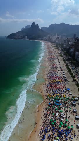 Aerial view of Ipanema Beach with colorful umbrellas, crowded sand, turquoise ocean waves, and Dois Irmaos mountains in Rio de Janeiro, State of Rio de Janeiro, Brazil.