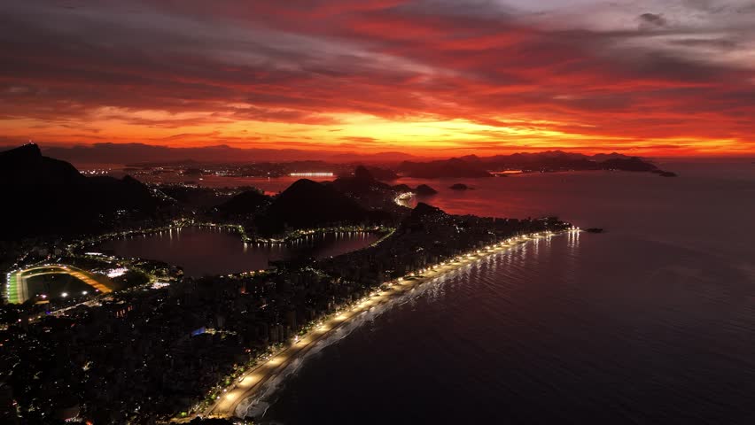 Aerial view of Rio de Janeiro coastline at sunset with illuminated city lights and dramatic orange sky in Rio de Janeiro, State of Rio de Janeiro, Brazil.