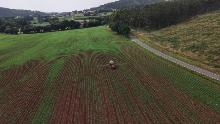 Agricultural tractor applying pesticide or fertilizer to young corn crops