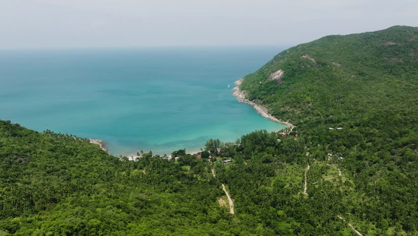 Drone view of a tranquil bay with turquoise water and forested green hills surrounding it. Bottle Beach. Ko Pha Ngan, Thailand.