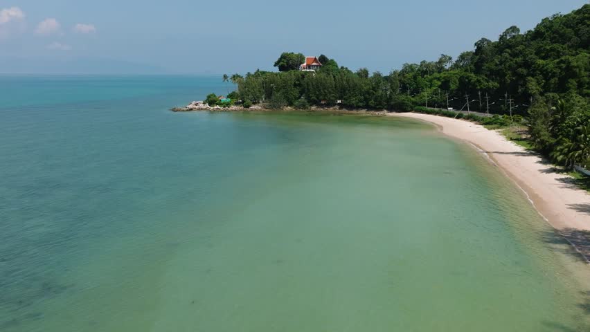 Sandy shoreline with a small temple situated on a lush green hill surrounded by turquoise ocean waters. Maenam Beach. Ko Samui, Thailand.