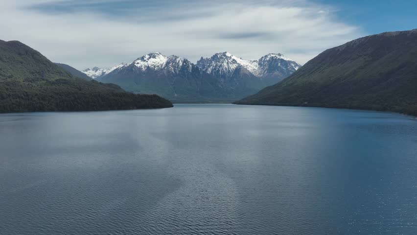 Scenic landscape featuring a wide view of snow-capped mountains reflecting on the calm, deep blue water of a vast lake