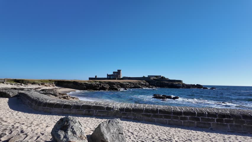 Stone seawall bordering a sandy beach on the Atlantic coastline of Trévignon, Brittany, France. Scenic summer coastal landscape featuring ocean waves, rugged shoreline and traditional seaside scenery on the French Atlantic coast.