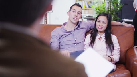 An attractive and happy young couple of mixed ethnicity are having a meeting with their bank manager or financial adviser. 