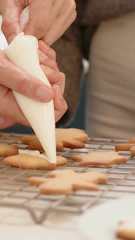 Vertical video: Squeezing hands holding piping bag after closeup, icing cookies at home in sweater. Baking, cookie, frosting, decorating, kitchen, homemade, vertical video