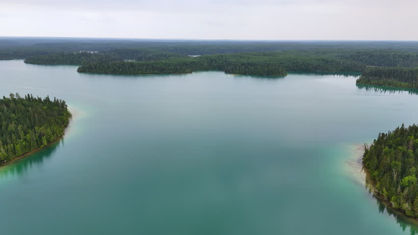 Aerial view of the expansive blue-green waters of Big Skunk Lake in northern Ontario, bordered by pristine boreal forest and untouched wilderness.