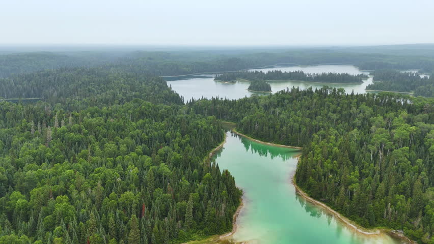 Aerial view of a narrow channel connecting two pristine lakes through dense boreal forest in northern Ontario, featuring striking emerald and turquoise water.