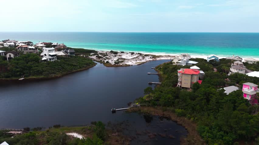 Aerial orbit over Draper Lake and its coastal inlet opening toward vivid turquoise Gulf bay and sandy Old Florida Beach shoreline, Florida, US