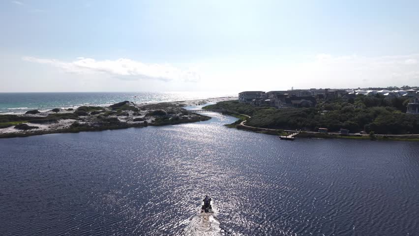 Drone overview fly of Camp Creek Lake inlet channel with sunlit reflecting on lake water top surface near shoreline community, Florida, US