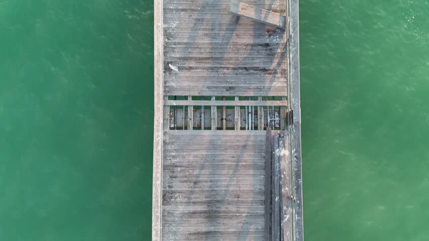 Aerial view of the weathered wooden planks of the historic Naples Pier surrounded by the calm turquoise waters of the Gulf of Mexico in Naples, Florida, United States.