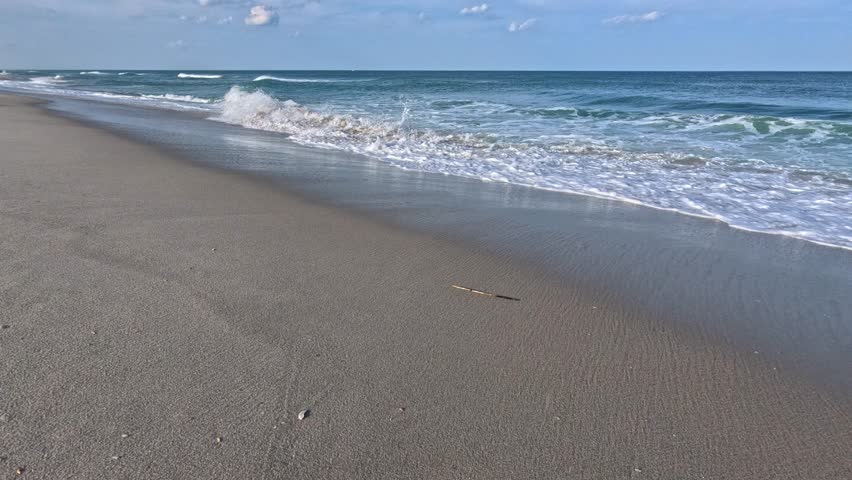 Island Beach State Park, New Jersey, USA: Landscape of a wide sandy beach along the Atlantic coast of New Jersey in Island Beach State Park. The calm Atlantic Ocean with gentle waves washes over the fine sandy shoreline. Sea foam is visible in the foreground, creating a peaceful, scenic, and tranquil coastal atmosphere.