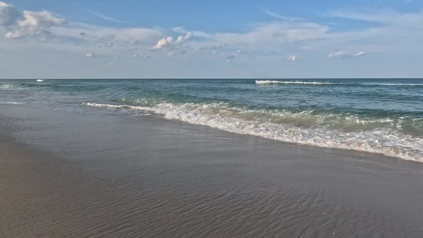 Island Beach State Park, New Jersey, USA: Landscape of a wide sandy beach along the Atlantic coast of New Jersey in Island Beach State Park. The calm Atlantic Ocean with gentle waves washes over the fine sandy shoreline. Sea foam is visible in the foreground, creating a peaceful, scenic, and tranquil coastal atmosphere.