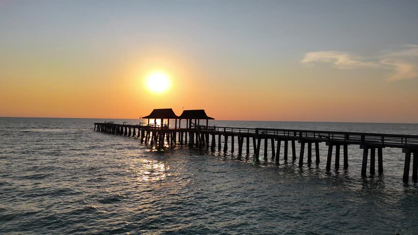 Aerial view of Naples Pier extending into the Gulf of Mexico during a golden sunset in Naples, Florida, United States.