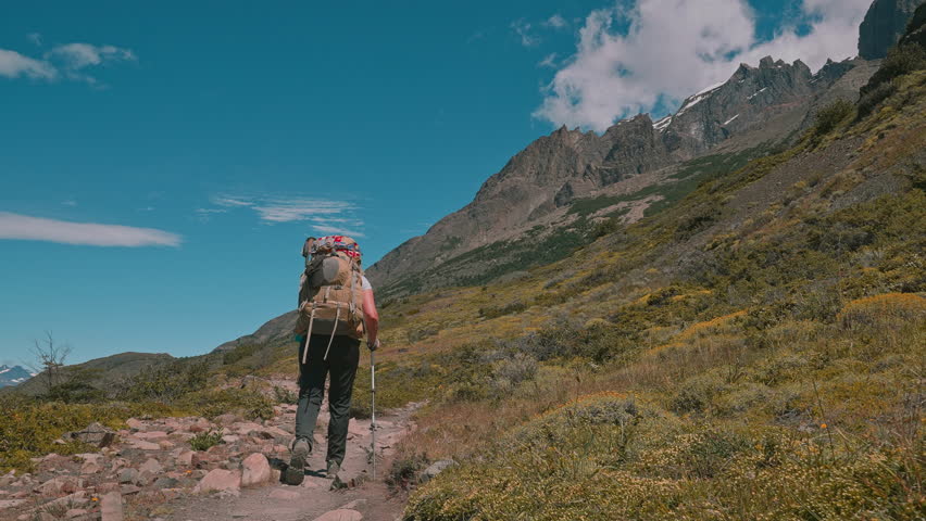 Following behind a backpacking hiker on the Torres del Paine W Trek with mountains and blue skies, Patagonia, Chile