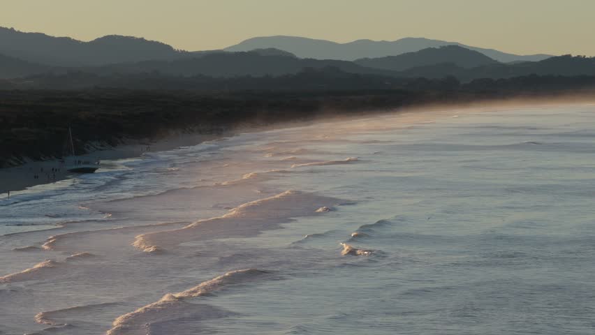 Aerial view of Belongil Beach with gentle waves rolling onto the sandy shore during golden hour in Byron Bay, New South Wales, Australia.