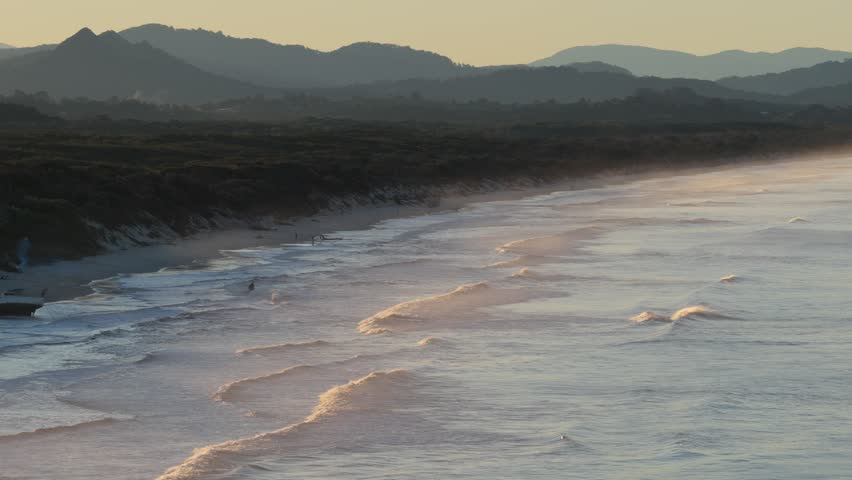 Aerial view of Belongil Beach with gentle waves rolling onto the sandy shore during golden hour in Byron Bay, New South Wales, Australia.