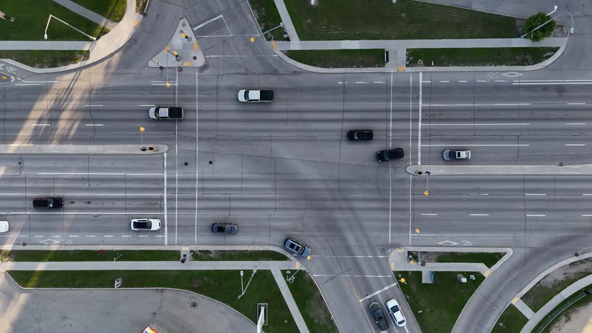 Drone aerial of a Winnipeg intersection, Manitoba, Canada ascending to reveal more roadway, cars, traffic lights, sidewalks, grass areas, and surrounding buildings.