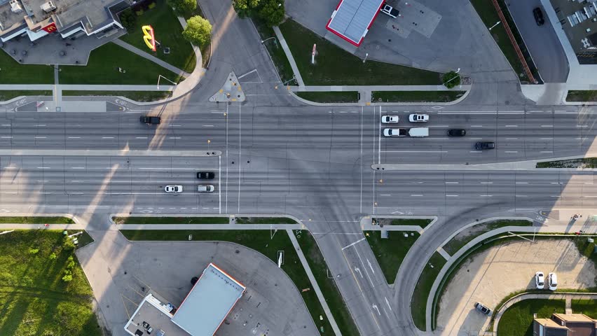 Drone aerial over busy Winnipeg intersection, Manitoba, Canada. Camera slowly descends toward road showing cars, streetlights, sidewalks, grass and surrounding buildings.