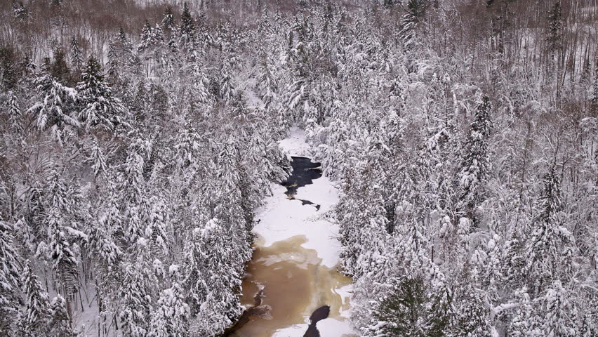 Aerial winter scenery featuring a snow-covered forest and partially frozen river in Northern Michigan.