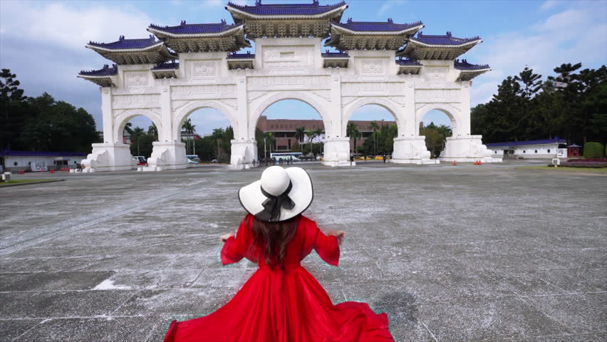 The Asian woman wearing a red dress is running toward the entrance of the Chiang Kai-shek Memorial Hall in Taipei, Taiwan.