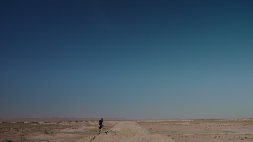 Small figure of man walking on dirt track across open desert plain in Morocco under wide blue sky