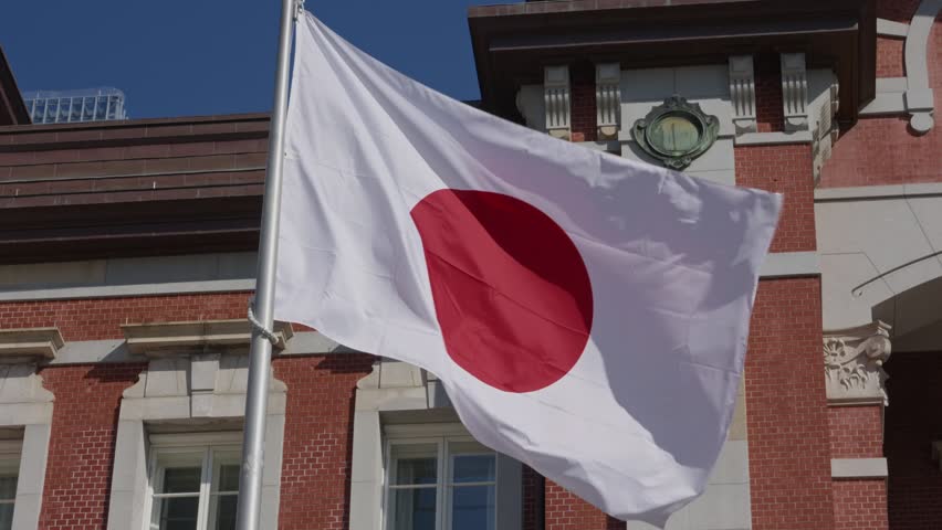 Japanese flag waving over historic red brick Tokyo Station facade in Tokyo Japan