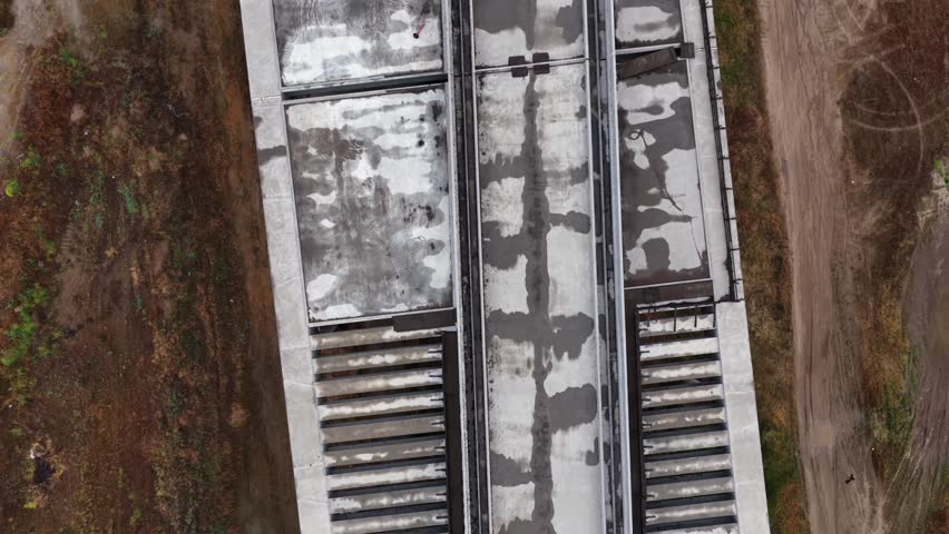 Concrete high-speed rail structure runs between dirt embankments near Fresno, California, USA, showing construction access road, exposed soil, circular ground patterns. Aerial drone top down shot