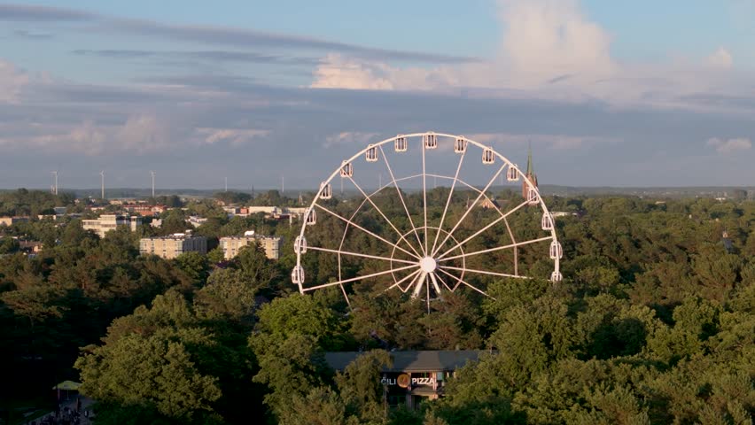 Aerial view of the Ferris wheel surrounded by lush green trees and a church spire in the distance in Palanga, Klaipeda County, Lithuania.