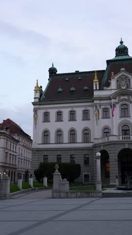 University of Ljubljana facade shows ornate entrance architecture and flags, vertical right pan shot.