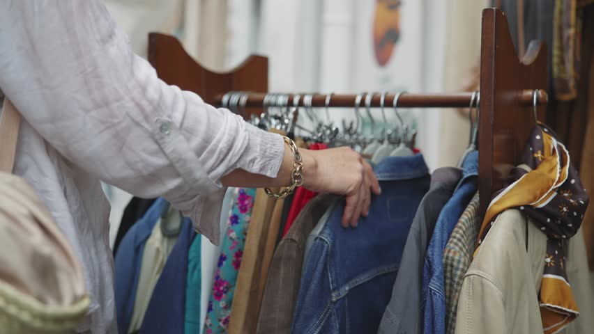 Female hand sifts through various clothes on a rack at an outdoor market stall. Authentic shopping scene in Palermo, Sicily, capturing real-life interaction.