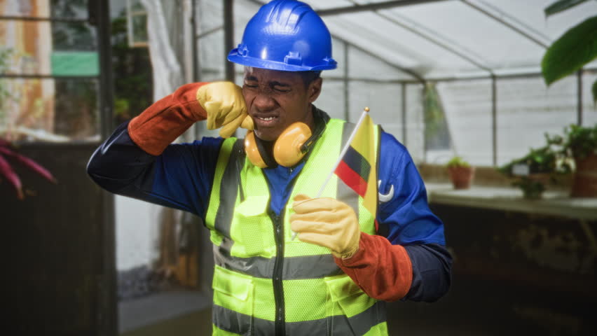 Man holding colombian flag and rubbing face in a building wearing hardhat and safety vest; patriotism duty fatigue.